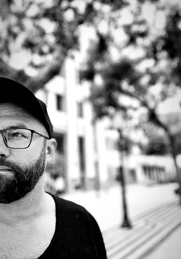 Ivo Deutschmann in a cap and glasses on a tree-lined street