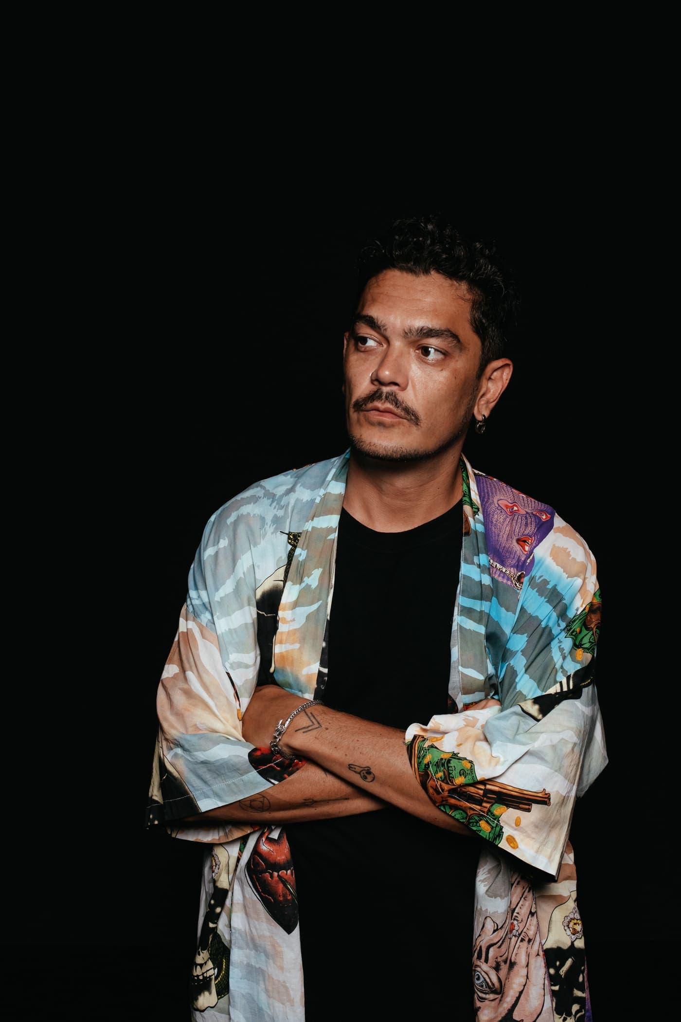 Kaiser Waldon in a patterned jacket, arms crossed, against black