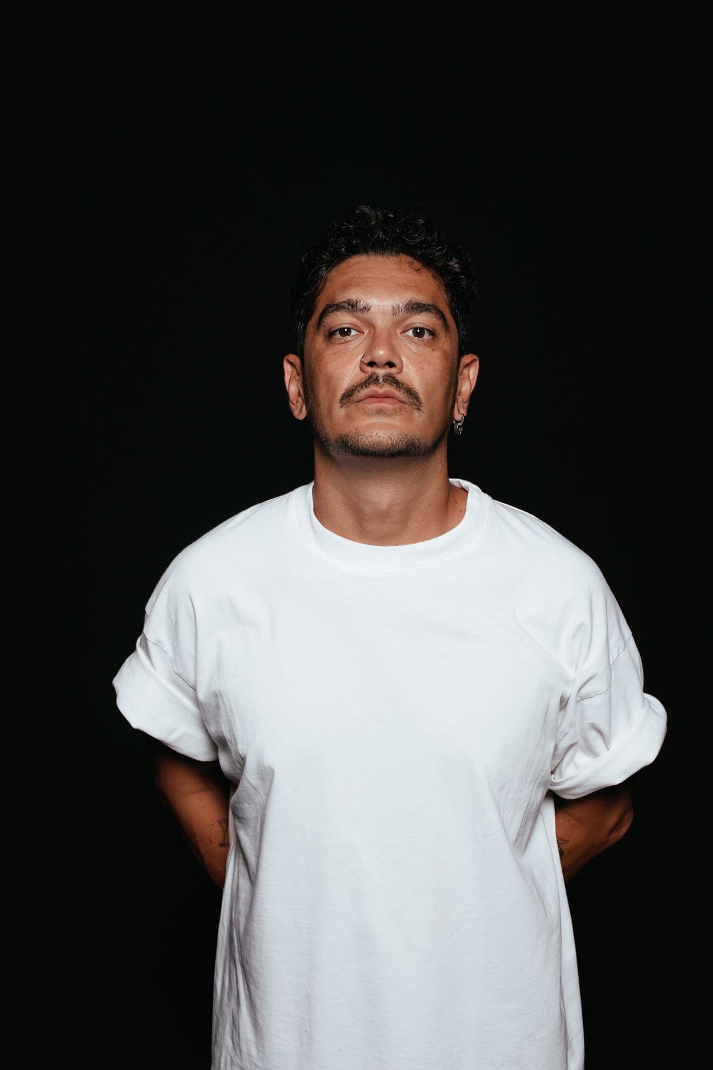 Kaiser Waldon in a white t-shirt, hands behind his back, against black