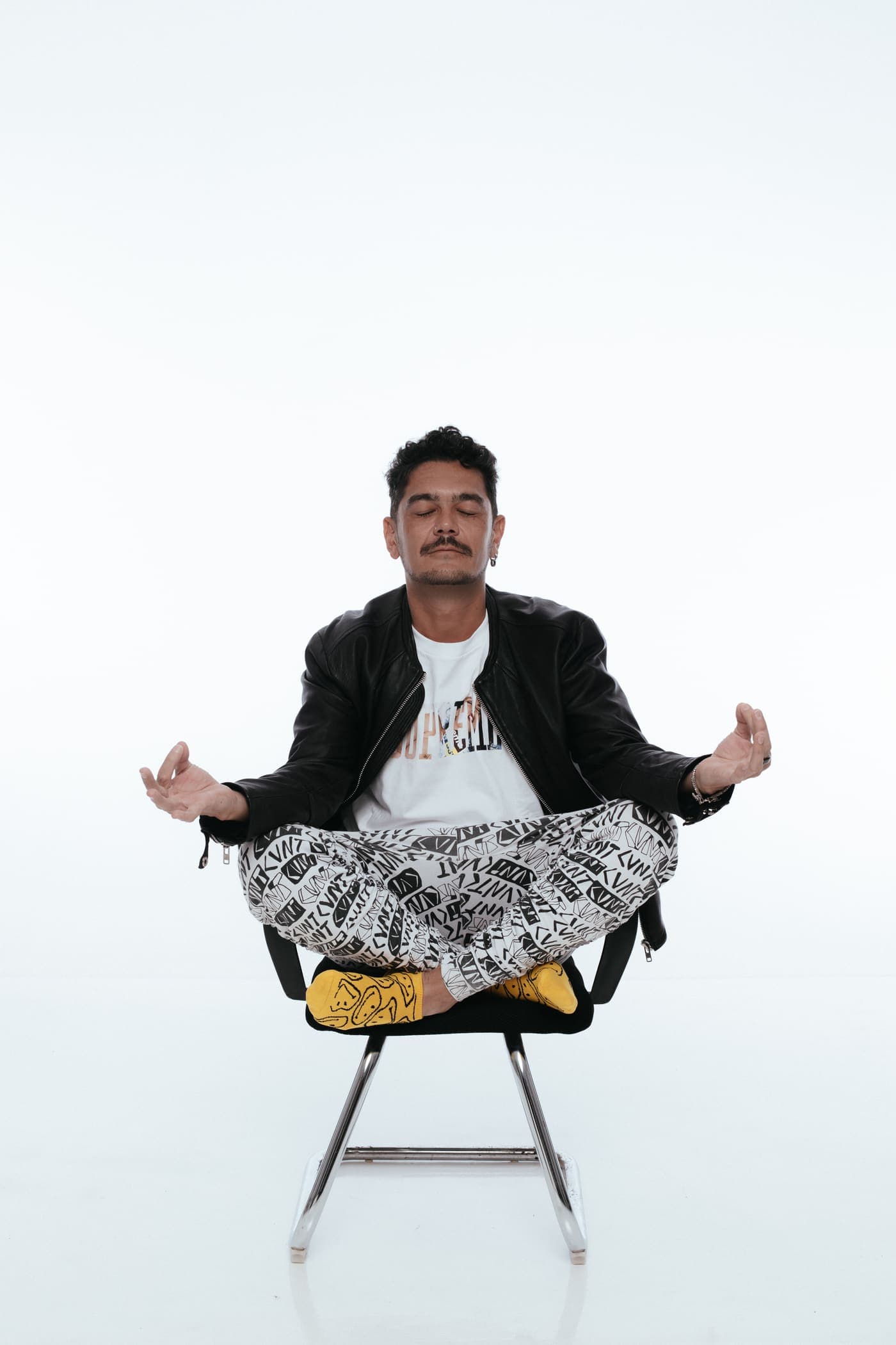 Kaiser Waldon seated cross-legged on a chair against black