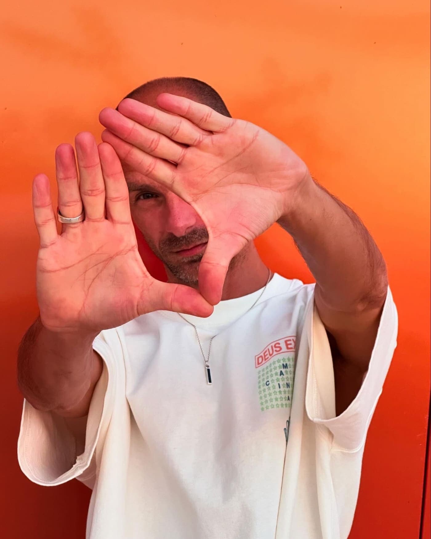 Max Hefele raising a hand towards the camera against an orange backdrop