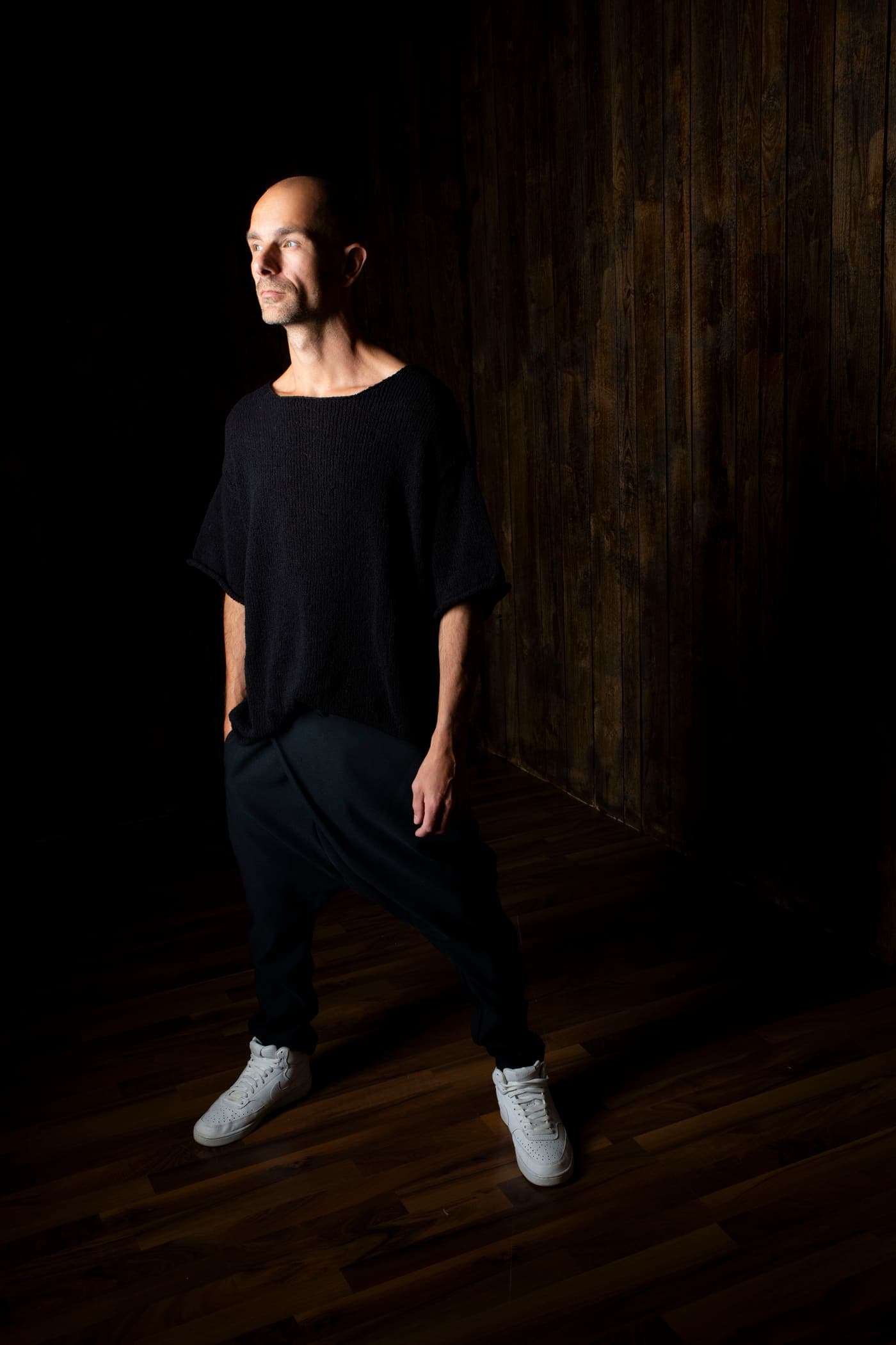 Max Hefele full length in a dark room with a wooden wall