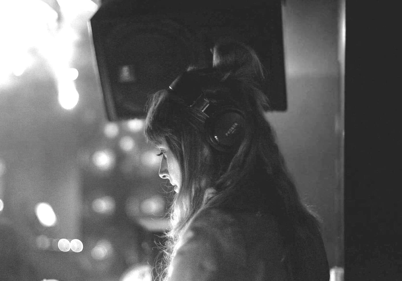 Juli Lee behind the decks in a dark room, lights behind her